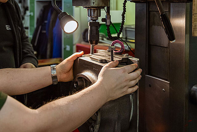 in der Metallwerkstatt bohrt ein Mitarbeiter Löcher in ein Getriebegehäuse