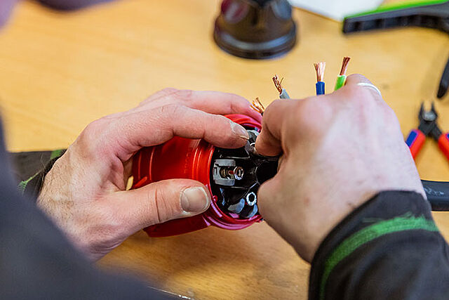 im Bereich der Kabelkonfektionierung verbindet ein Mitarbeiter ein Elektrokabel mit zugehörigen Stecker zu einem fertigen Stromkabel